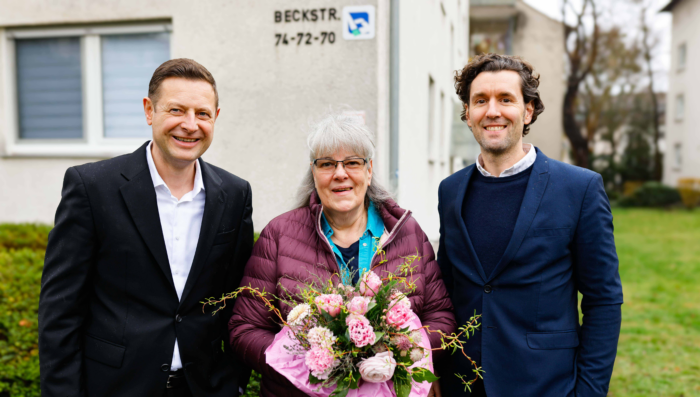 ENTEGA-Kundin Gabriele Illi freut sich über den ersten Glasfaseranschluss in einer Bauvereinsimmobilie. Christoph Busch, ENTEGA Medianet-Geschäftsführer (li.), und Stefan Backmund, Bereichsleiter des Bestandsmanagement der bauverein AG, überreichten ihr anlässlich der offiziellen Inbetriebnahme einen Blumenstrauß